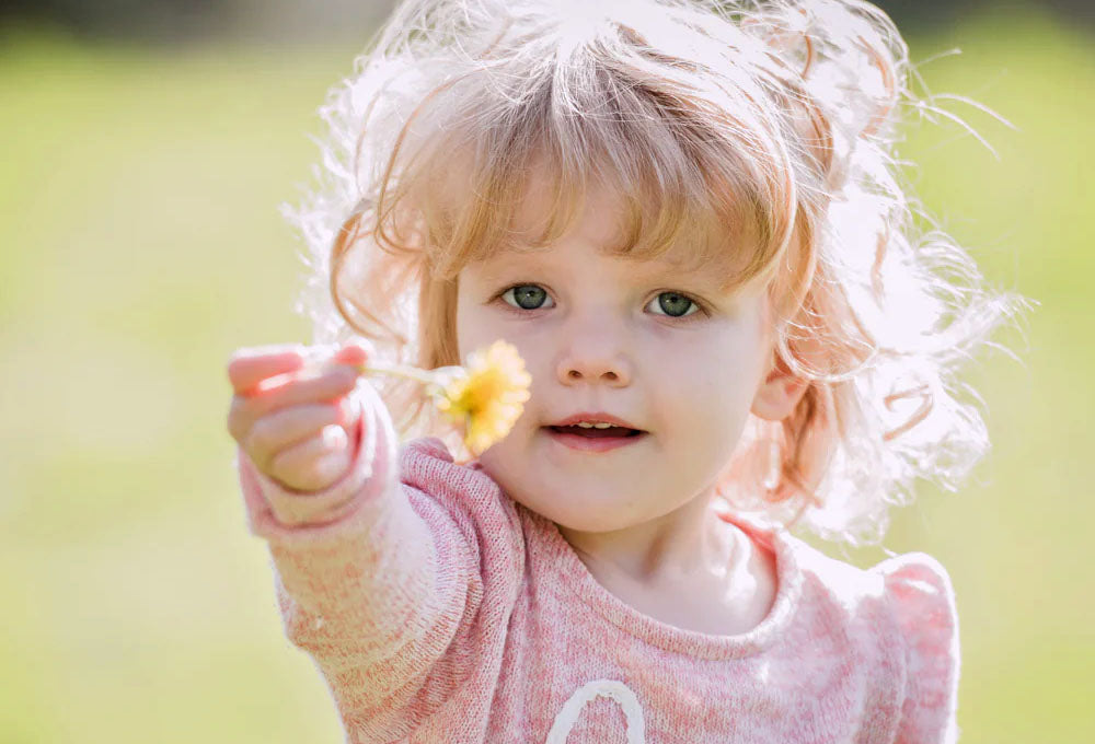 young girl with blond hair and blue eyes wearing a pink jumper holding a yellow follow out in front of her.