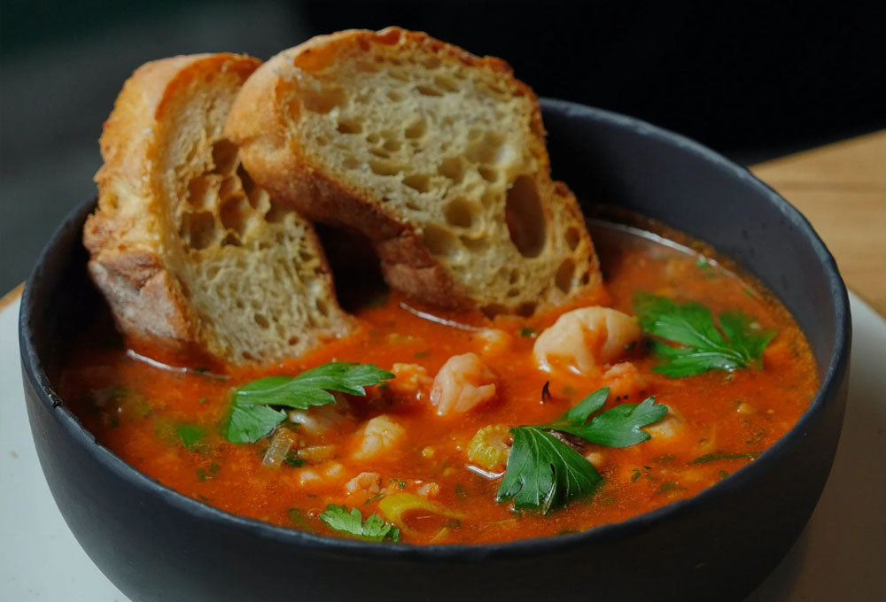 Abrey ceramic bowl with tomato and vegetable soup and two slices of white crust bread in it.