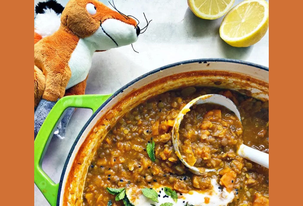 Lentil dahl in a casserole pot with a ladel inside and a soft toy next to it.
