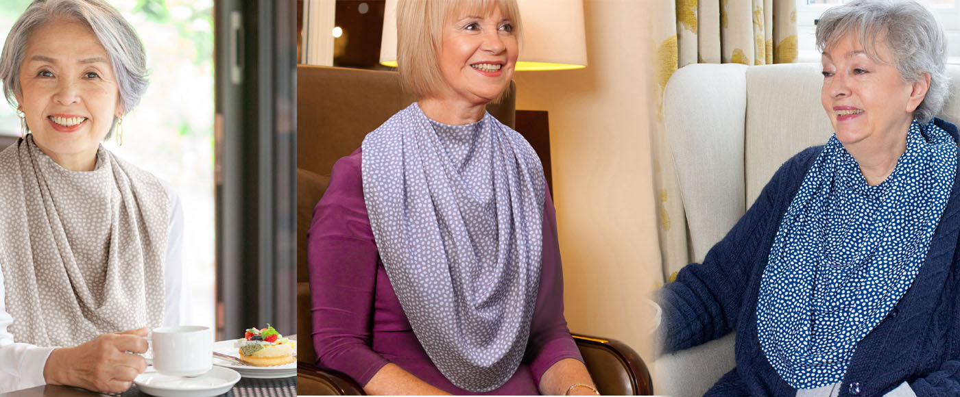 Three older women wearing Care Designs pashmina-style scarf clothing protectors in patterned fabrics, seated in home and café settings, smiling and relaxed.