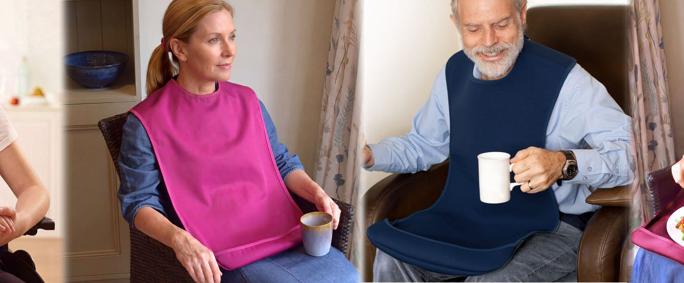 Four people seated from a teenager to elderly person wearing the range of Care Designs tabard style adult bibs either in navy or burdundy