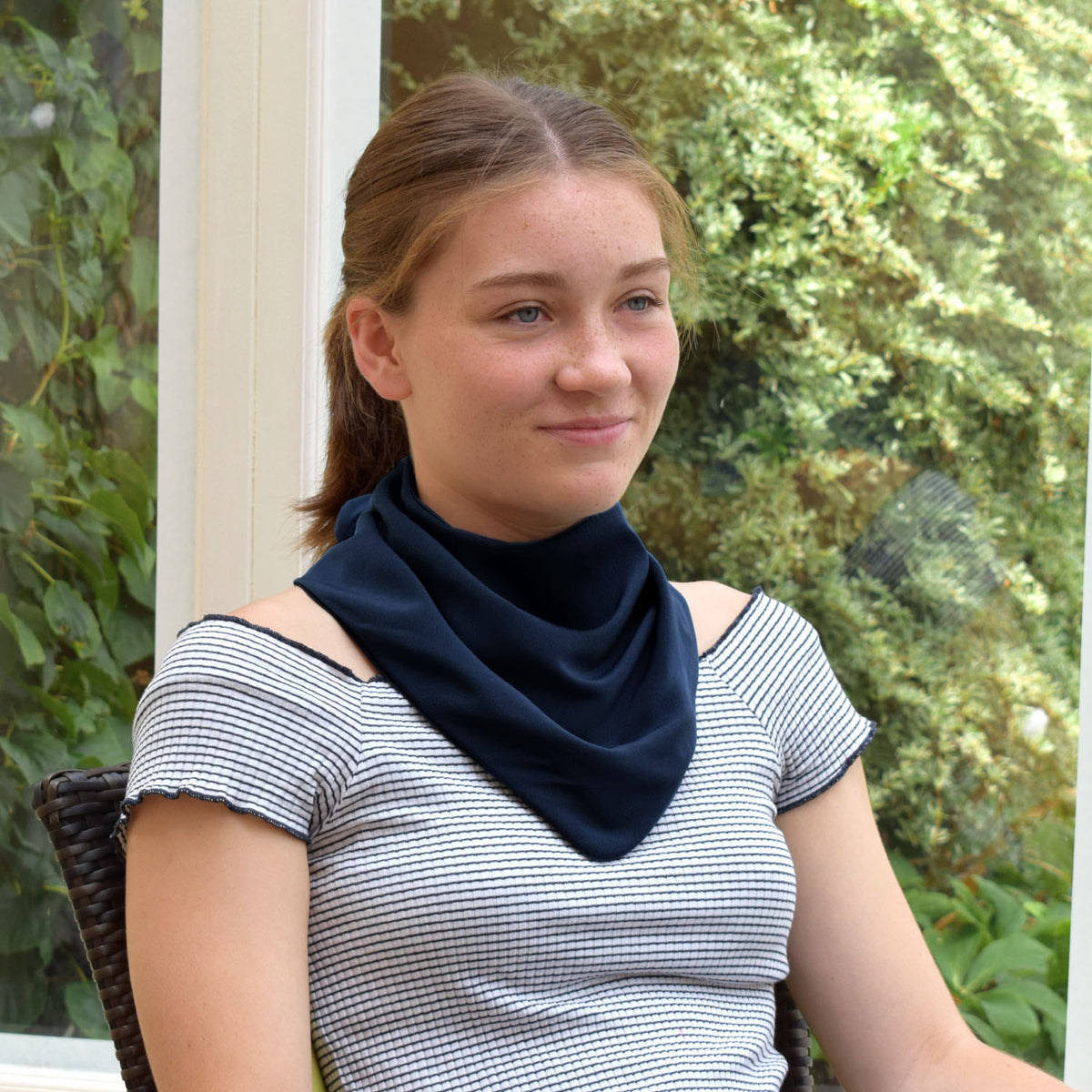 Teenager wearing a black neckerchief bib outdoors with greenery in the background