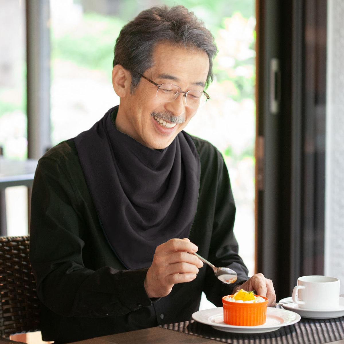 Man wearing a long black neckerchief bib eating dessert with a spoon at a table