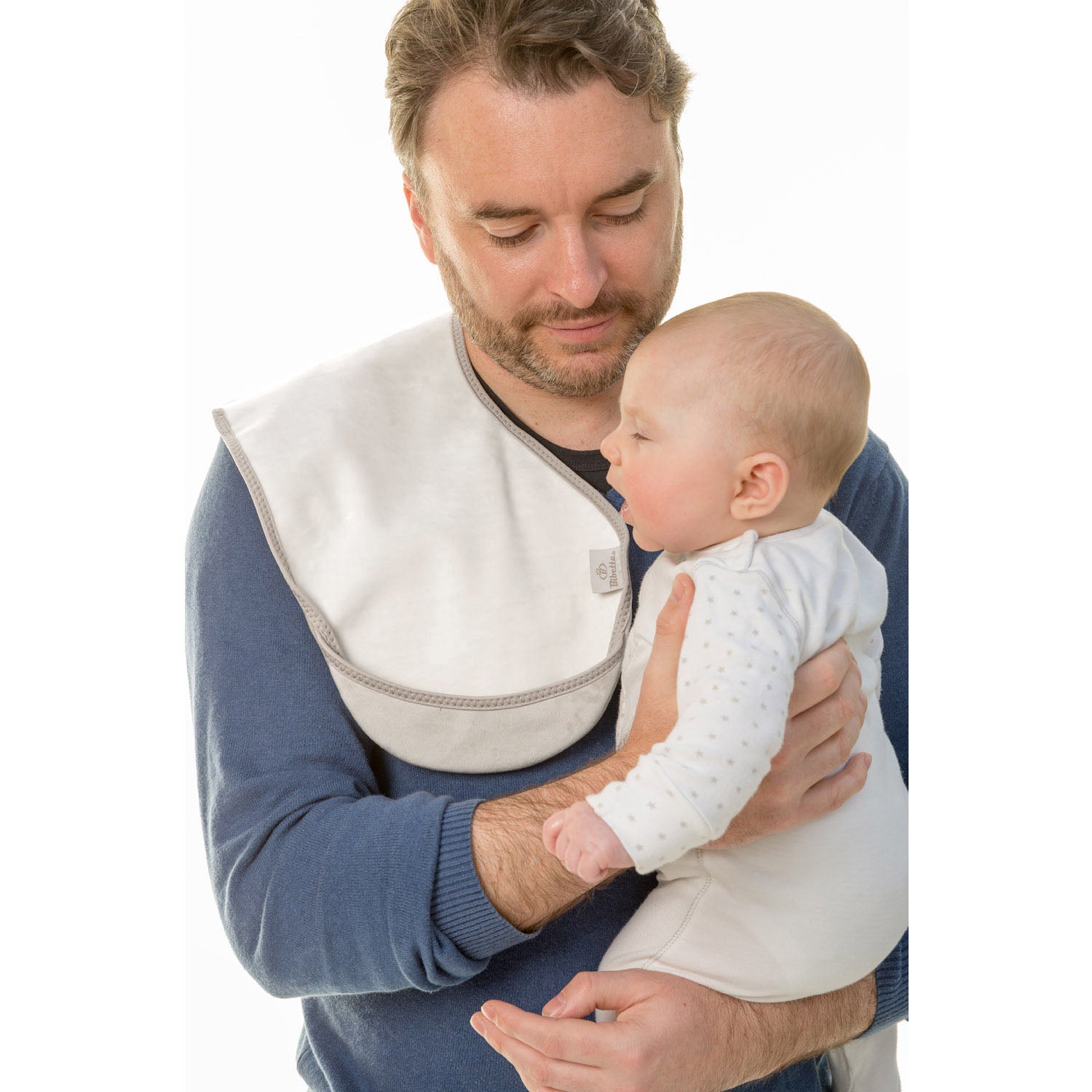man with brown hair wearing a blue long sleeve  top holding a baby in a white and grey spotted onsie with a Bibetta white and grey burp cloth on his shoulder