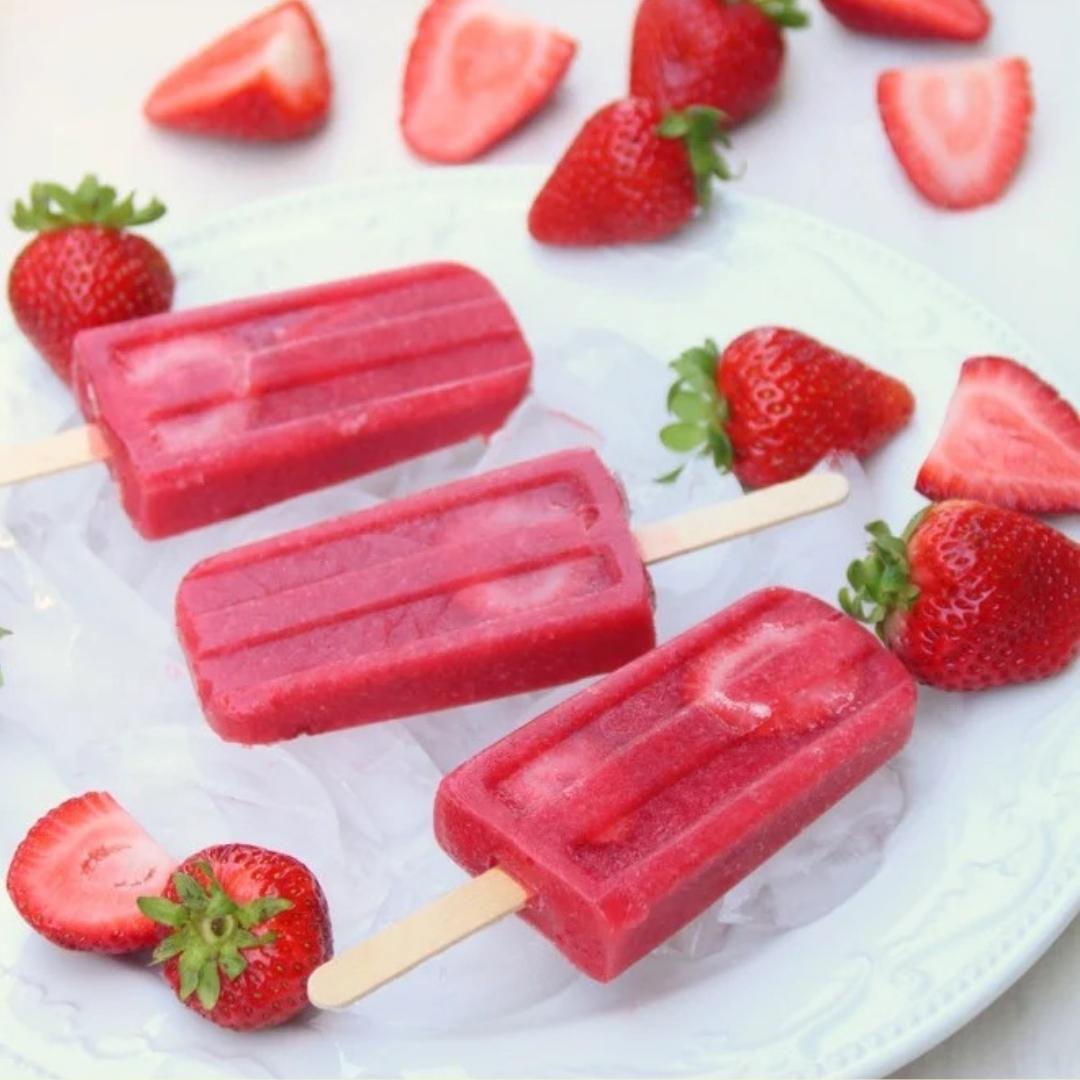 Strawberry ice lollies and strawberries lying on ice on a plate 