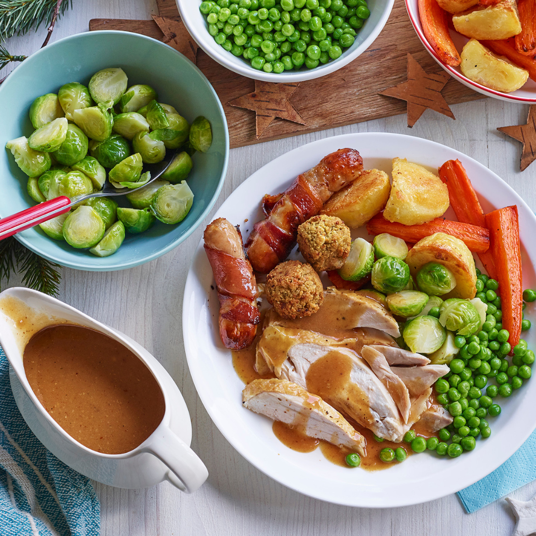 Traditional Christmas dinner, slices of turkey, peas, sprouts, carrots, roast potatoes, stuffing balls, sausages wrapped in bacon on a plate.