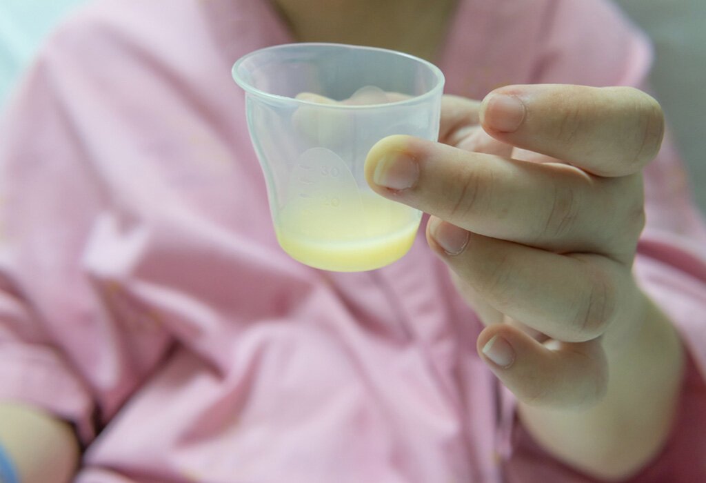Lady in a pink night gown holding a cup of colostrum
