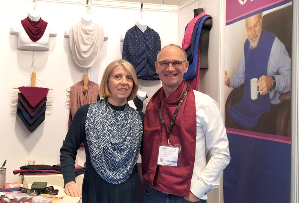 A lady  and gentleman modelling our scarf style clothing protectors at Care Designs by Bibetta stand at Naidex 2026 at the NEC, Birmingham