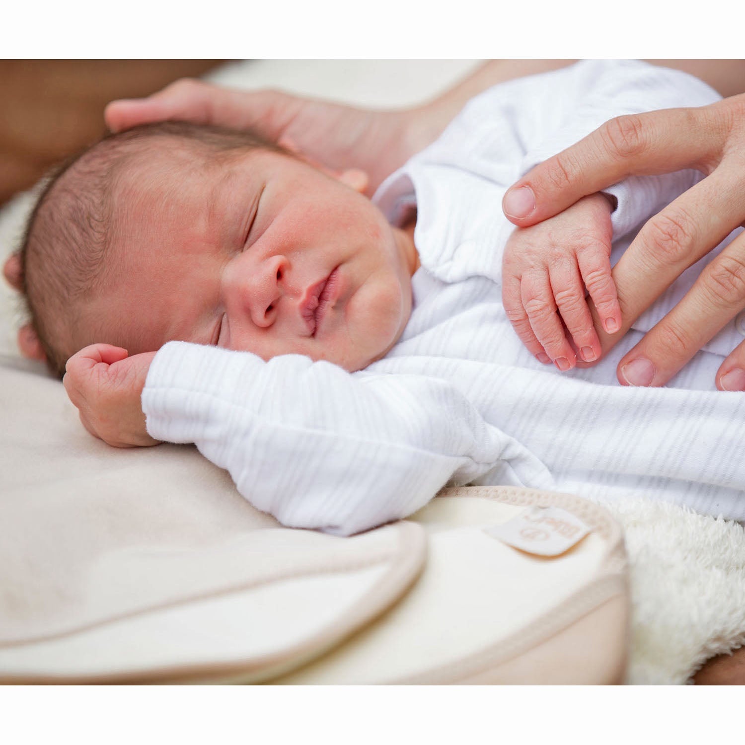 baby in a white sleepsuit lying down sleeping next to a Bibetta cream burpcloth