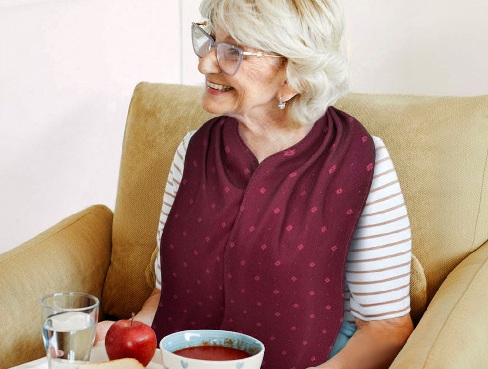 A Care Designs by Bibetta Straight Scarf style adult bib clothing protector in burgundy colour on a senior woman. A stylish, elegant and dignified design which is absorbent and has a waterproof backing for protection at mealtimes and throughout the day.