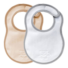 Two bibetta newborn plush bibs, one cream and beige with beige  bias binding and one white and grey baby bib with a grey bias binding with a zig-zag stitch and a teddy embossed in the front on a white background