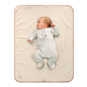 Baby in white sleep suit with bird motif on the front of it lying on a Bibetta cream and beige tummy time mat