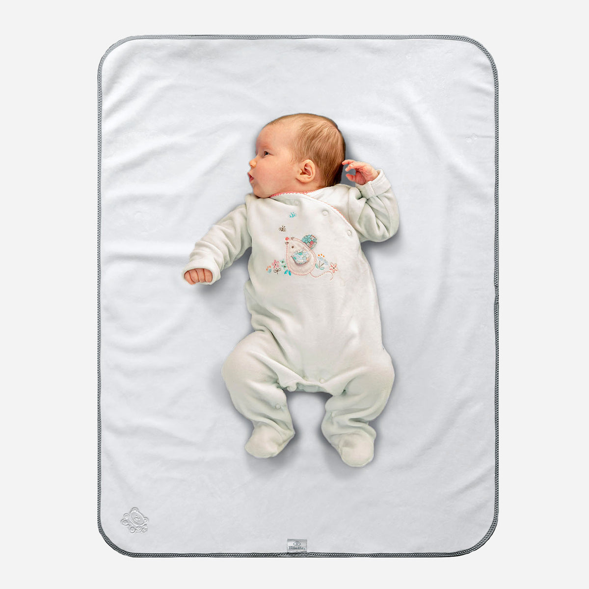 Baby in white sleep suit with mouse motif on the front of it lying on a Bibetta white and grey tummy time mat