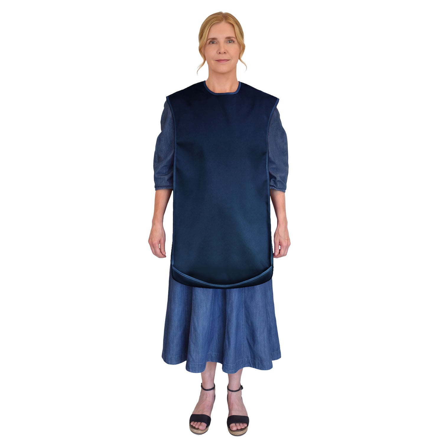 A woman modeling a long-sleeved, asymmetrical dress with a Care Designs large navy tabard adult bib, shown against a plain white background.
