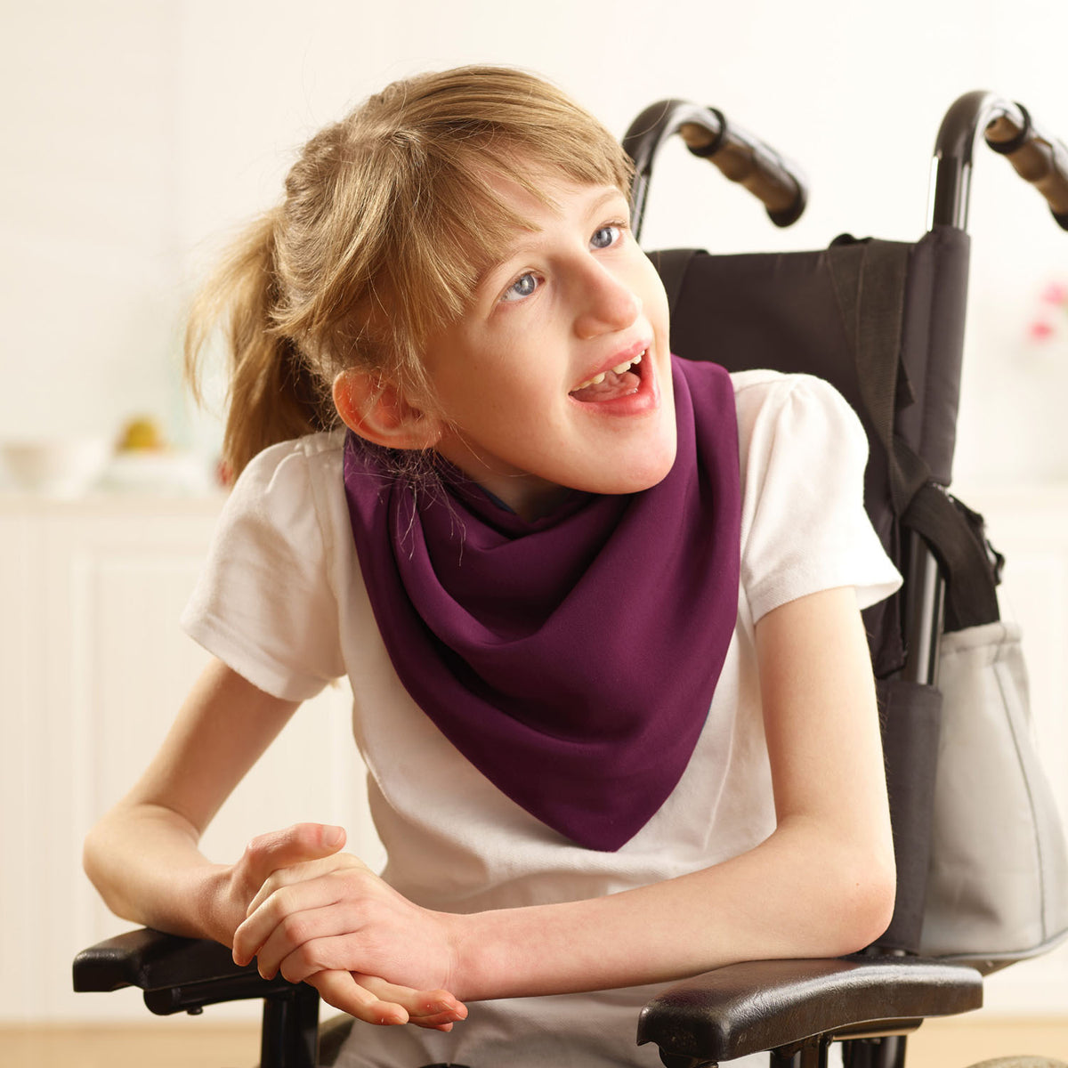 Young girl in a wheelchair wearing an aubergine neckerchief bib, looking up.