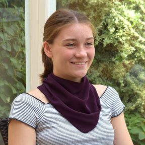 Teenager wearing an aubergine neckerchief bib outdoors with greenery in the background