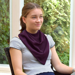 Teenager wearing a long aubergine neckerchief bib sitting outdoors with greenery in the background