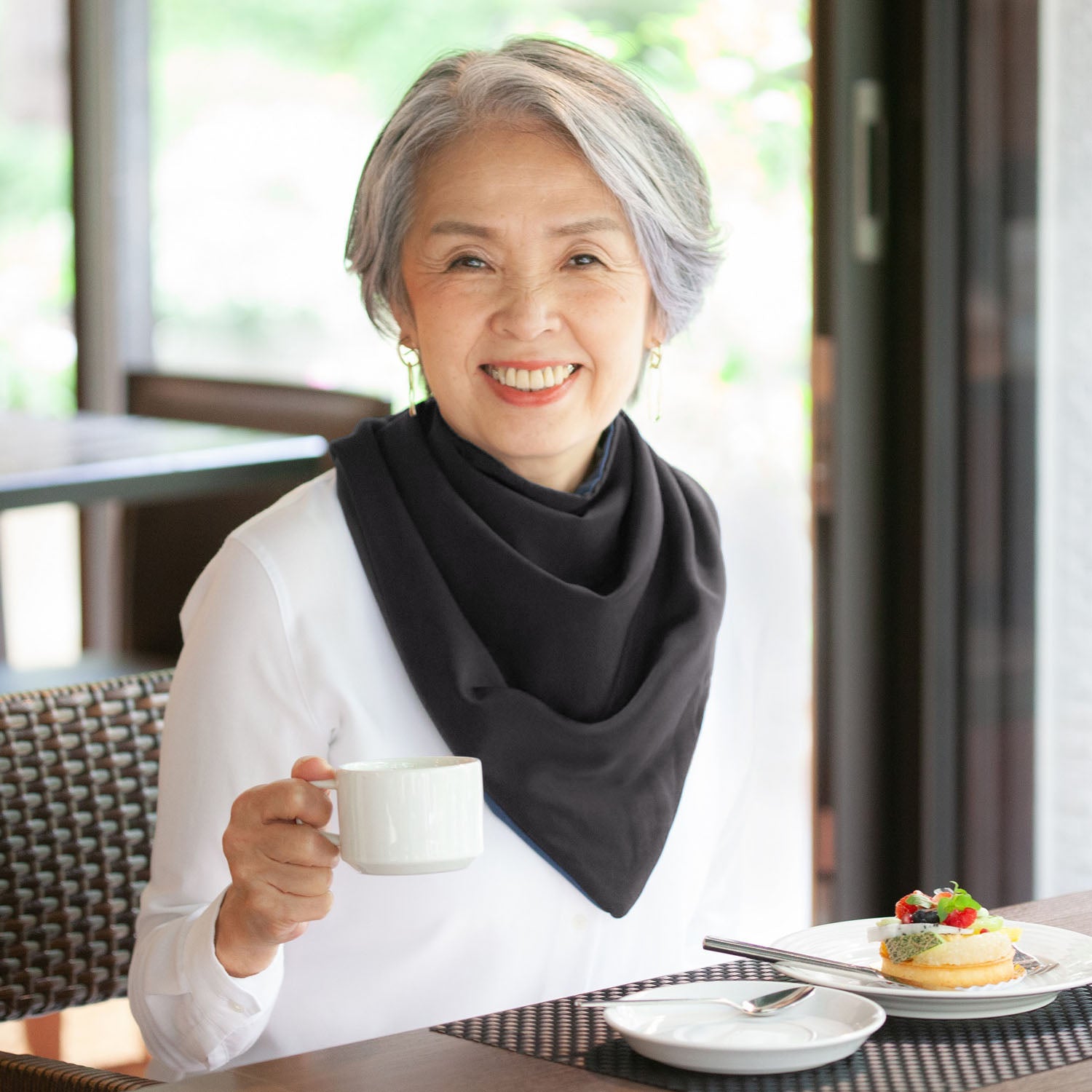 Woman wearing a long black neckerchief bib holding a cup of coffee in a cafe setting
