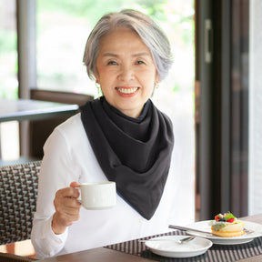 Woman wearing a long black neckerchief bib holding a cup of coffee in a cafe setting