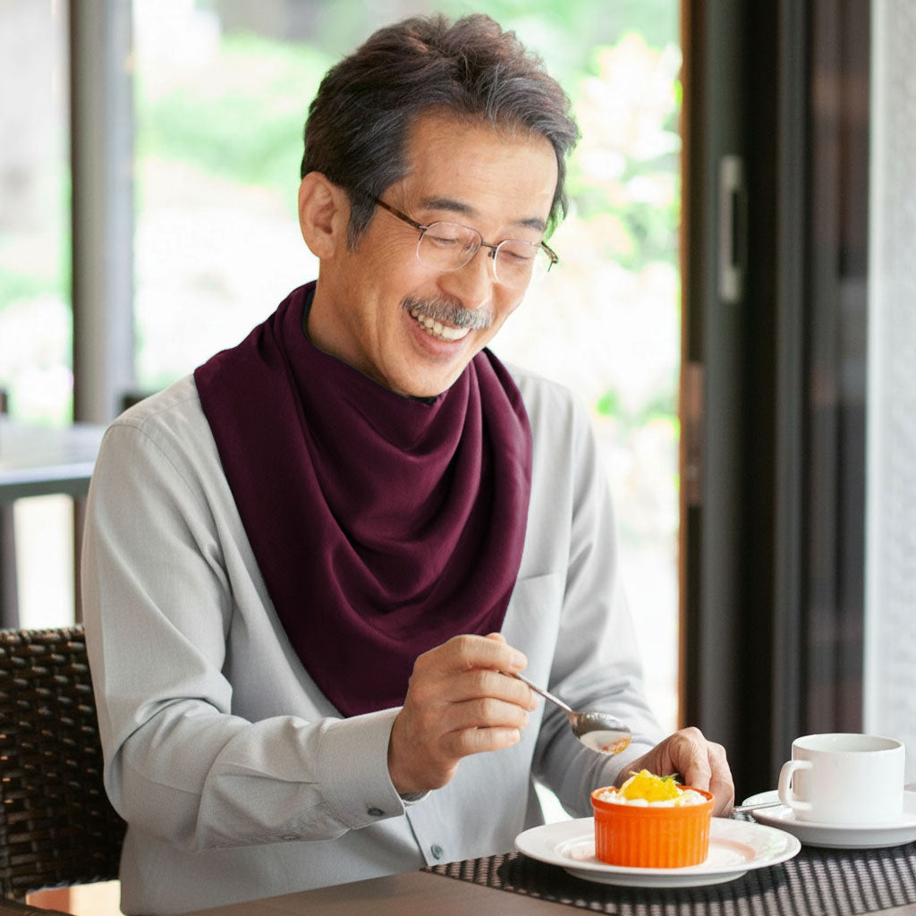 Man wearing a long burgundy neckerchief bib enjoying dessert outdoors with a cup of coffee