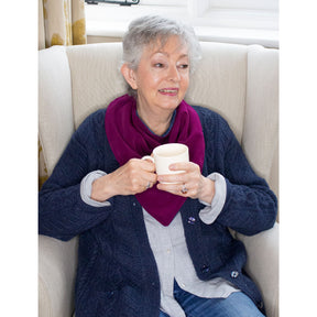 Woman sitting in a chair holding a mug, wearing a dark blue cardigan and long burgundy neckerchief bib