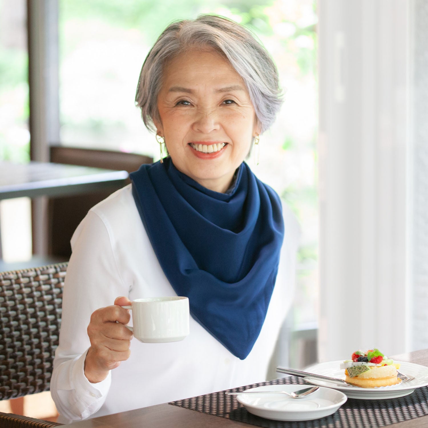 Woman wearing a long navy neckerchief bib holding a cup of coffee in a restaurant setting