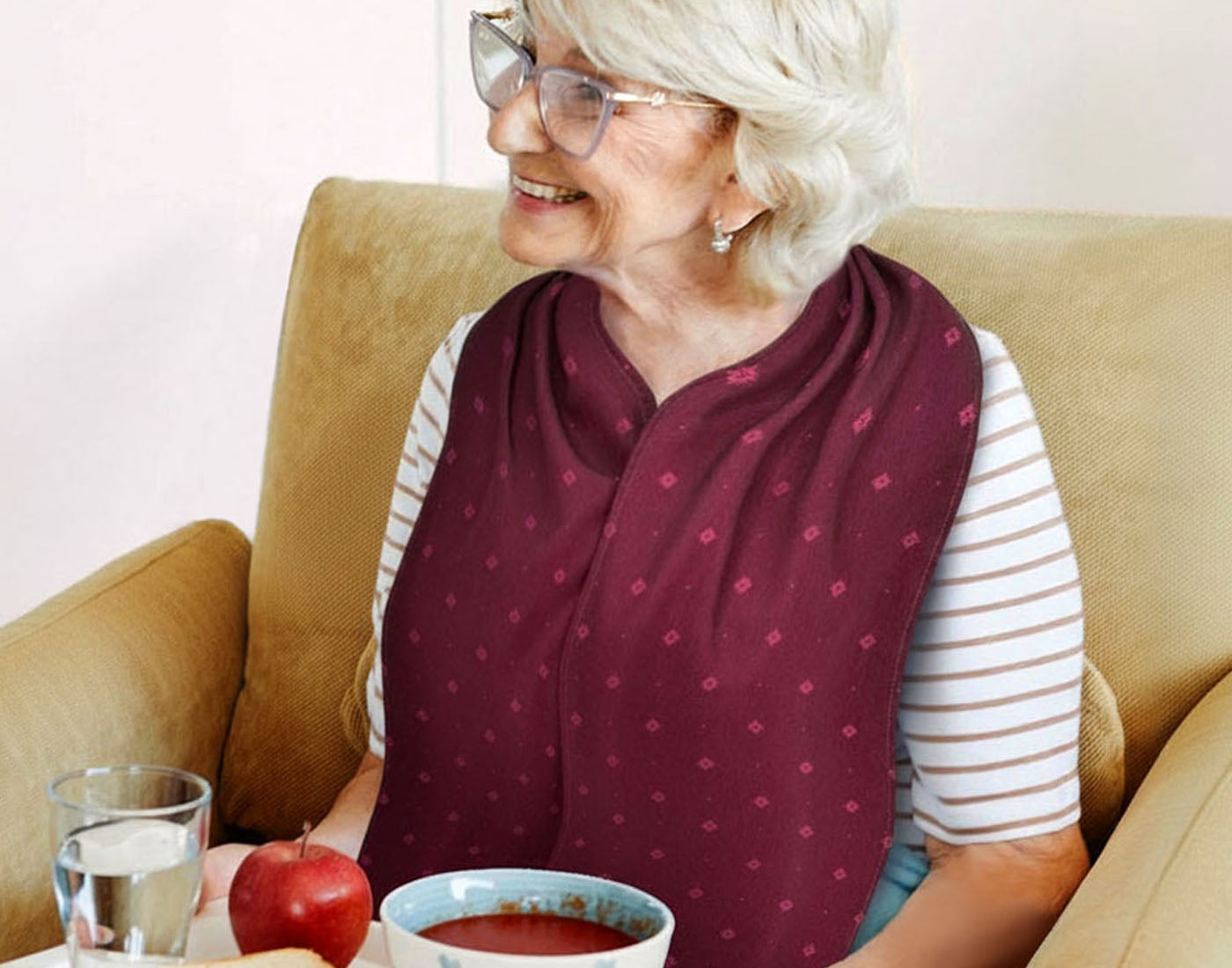 Senior woman wearing a stylish and dignified Care Designs, burgundy, straight scarf style, adult bib clothing protector whilst eating.