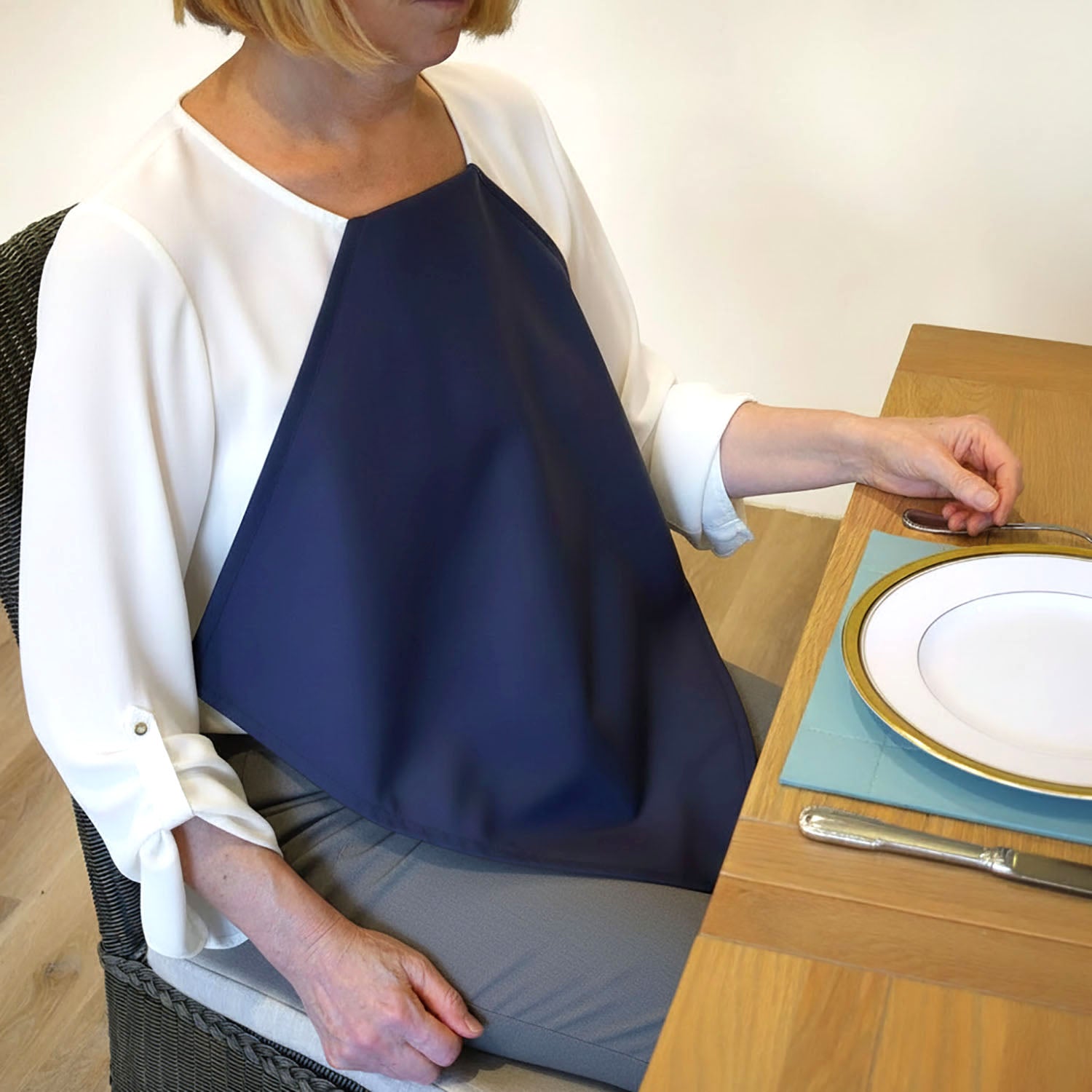 Woman wearing a Care Designs navy waterproof napkin over a white blouse at a dining table with a colorful placemat.