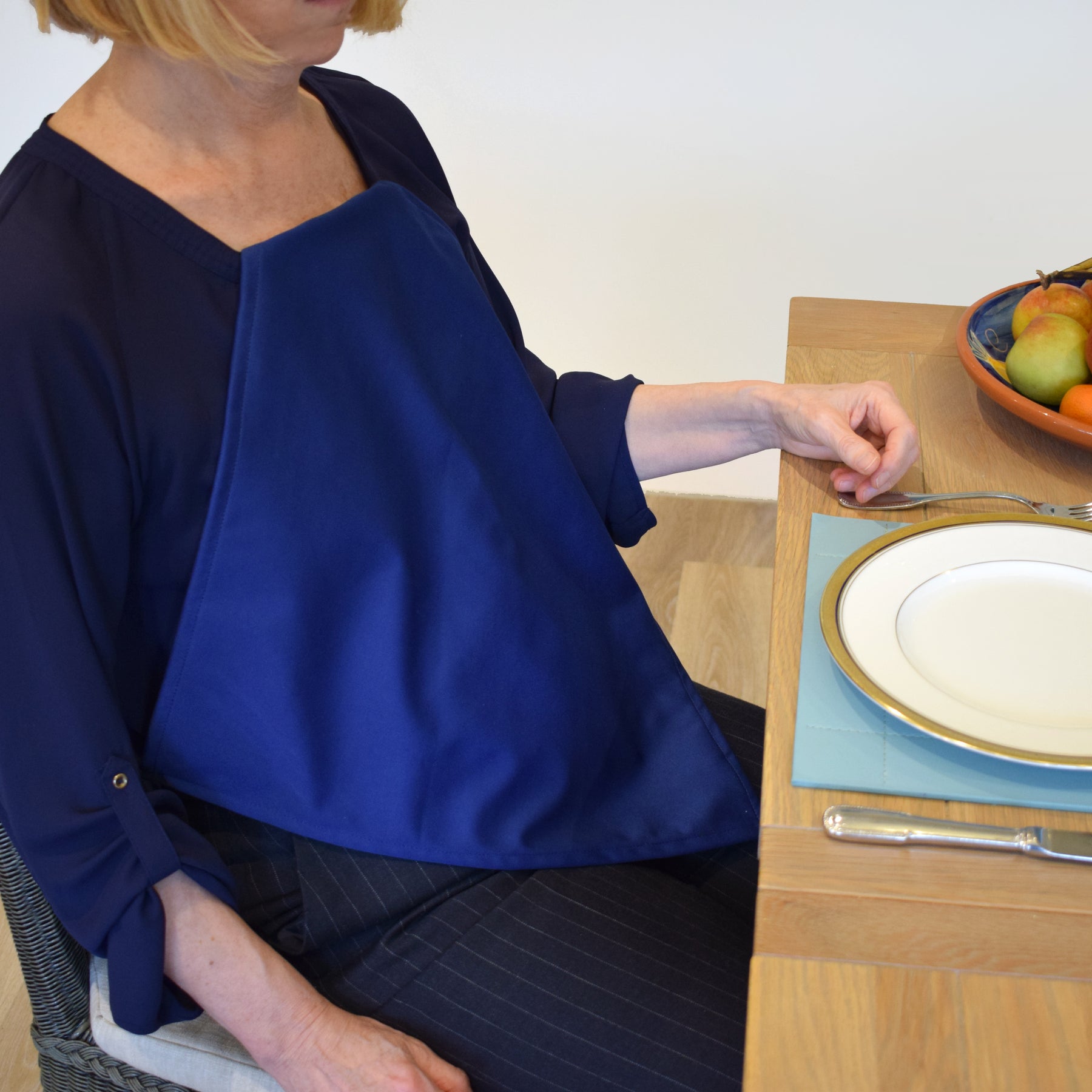 Person sitting at a table with a plate and fruit bowl waering a Care Designs navy waterproof napkin 
