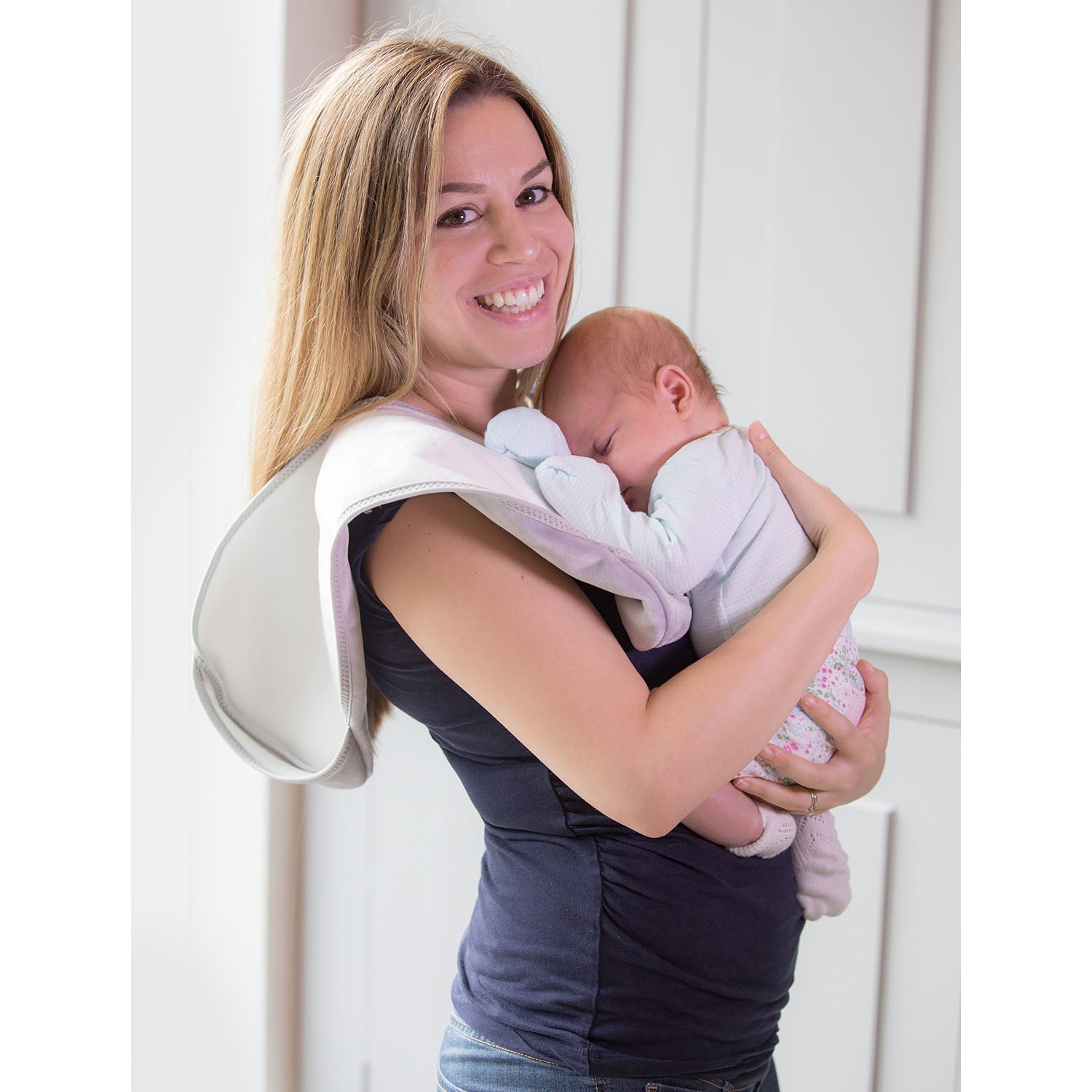 lady with brown hair wearing a long blue t-shirt holding a baby against her shoulder in a light blue top and flower leggings and pick socks with a Bibetta white and grey burp cloth 